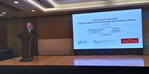 Thomas Alexander Hövelmann at a podium next to a projected presentation presenting his paper 'Path Expressions Revisited - Towards Compiler-enforced Reusable Synchronization Patterns' at the PLOS25 workshop.